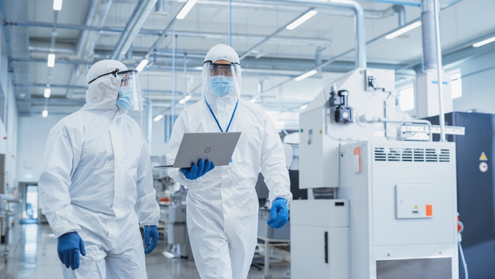 Two Scientists Walking in a Heavy Industry Factory in Sterile Coveralls and Face Masks